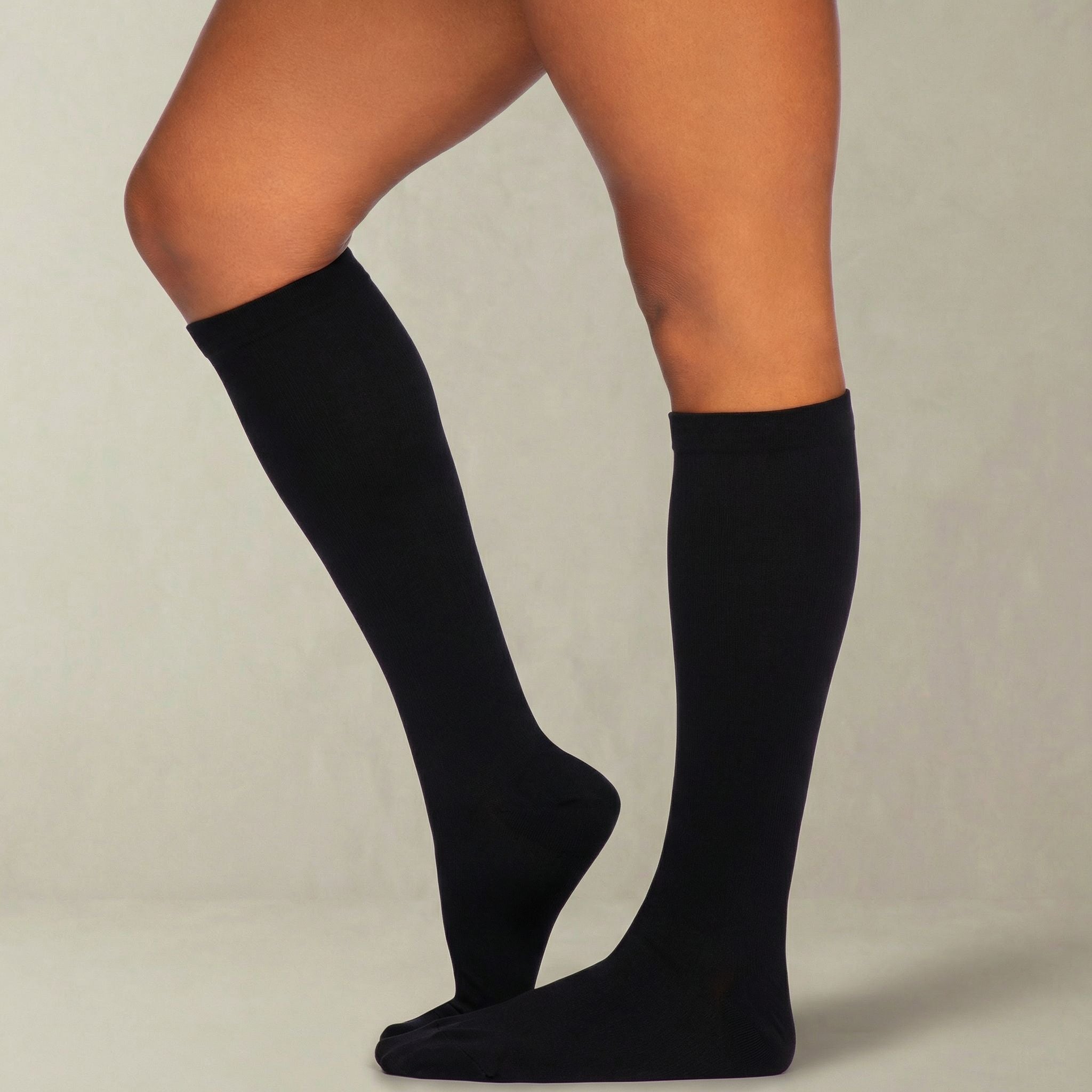 Black knee-high compression socks worn by a person on a neutral background
