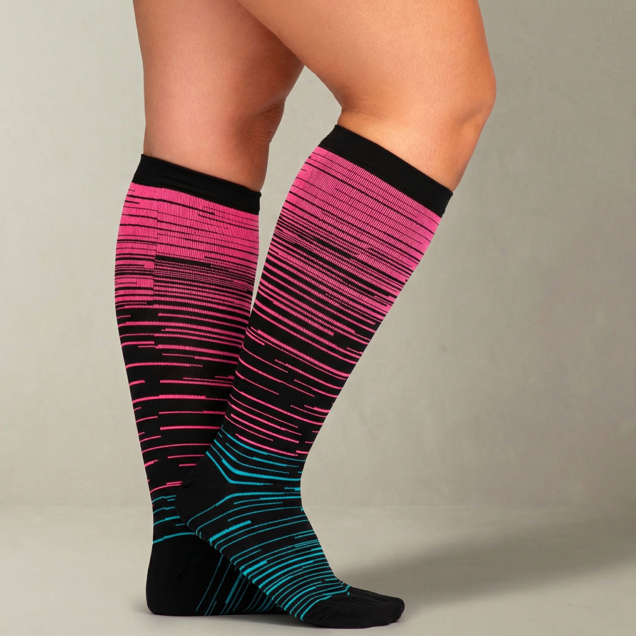 Pink and black striped compression socks worn by a person on a neutral background