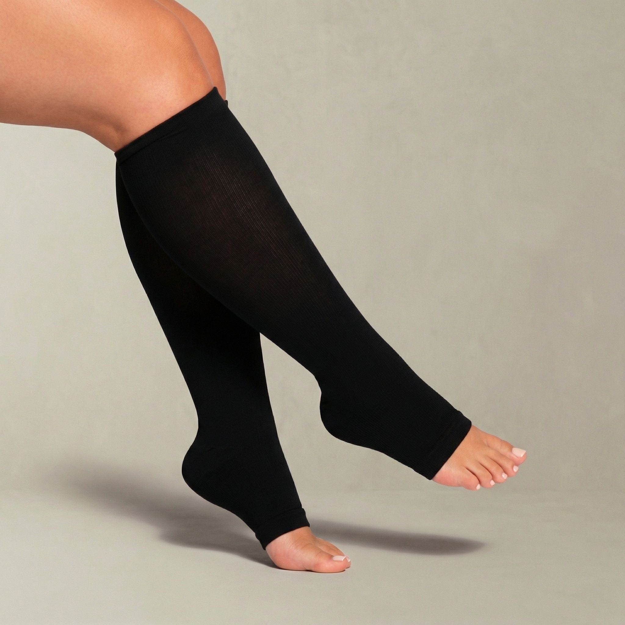 Person wearing black compression stockings on a plain background