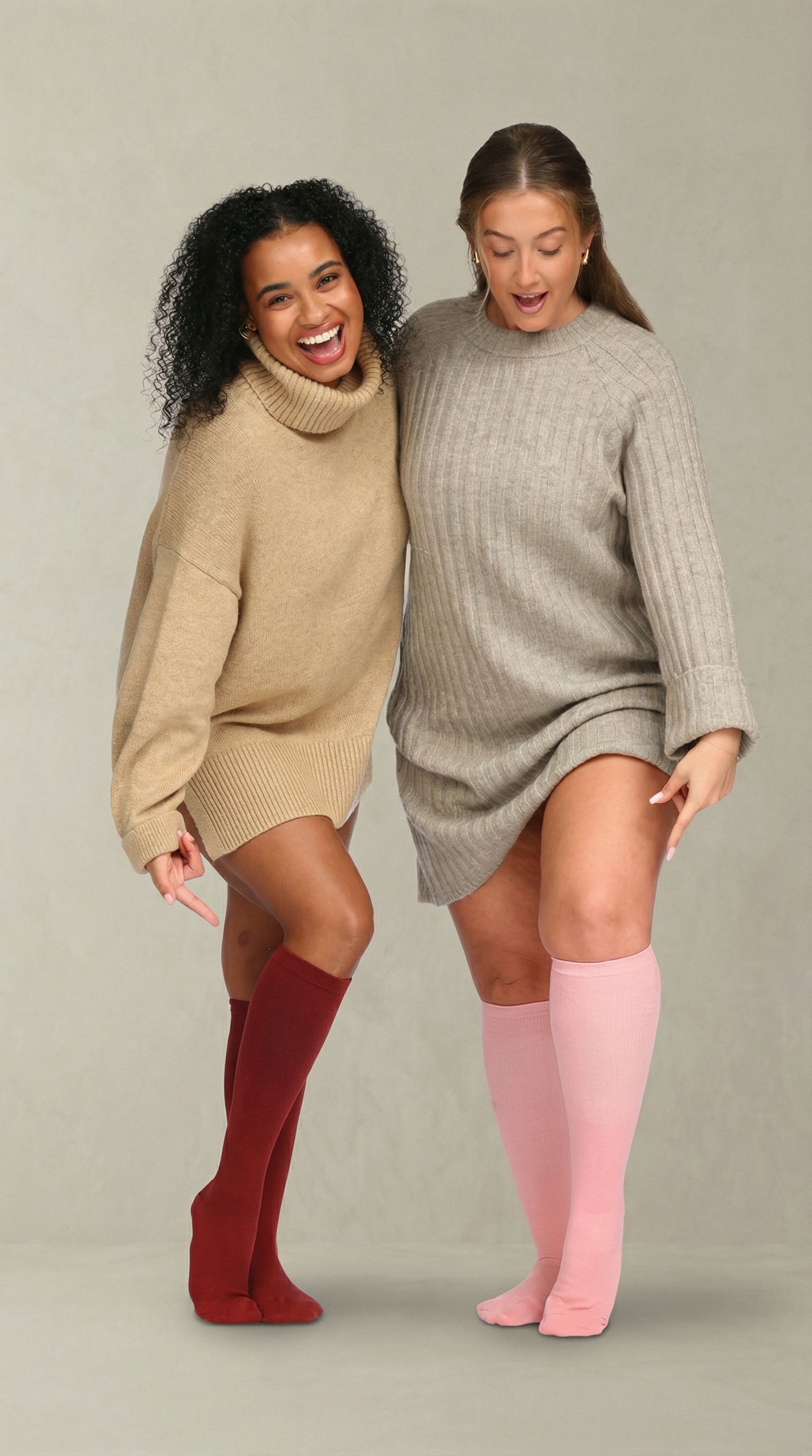 Two women wearing oversized sweaters and knee-high compression socks on a plain background