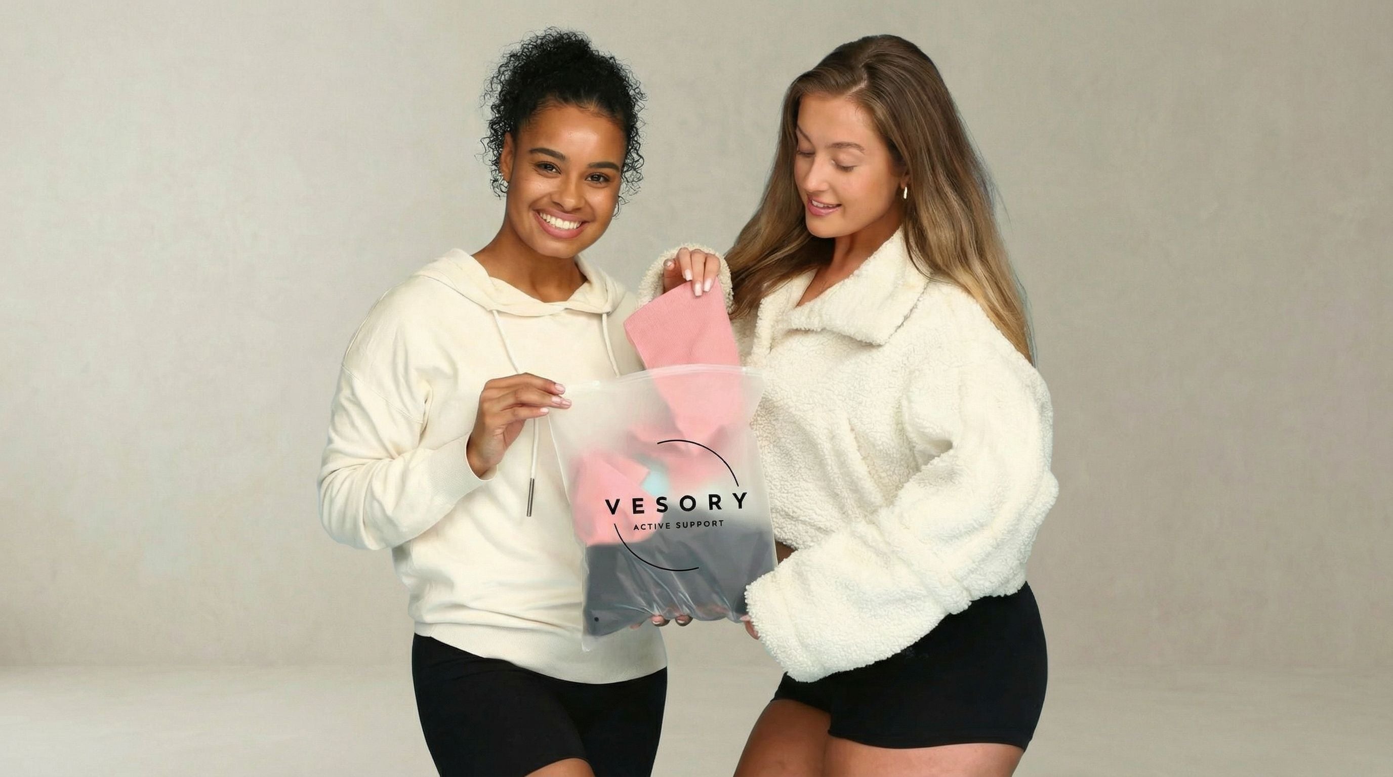 Two women holding a pink 'Vesory' compression sock against a plain background