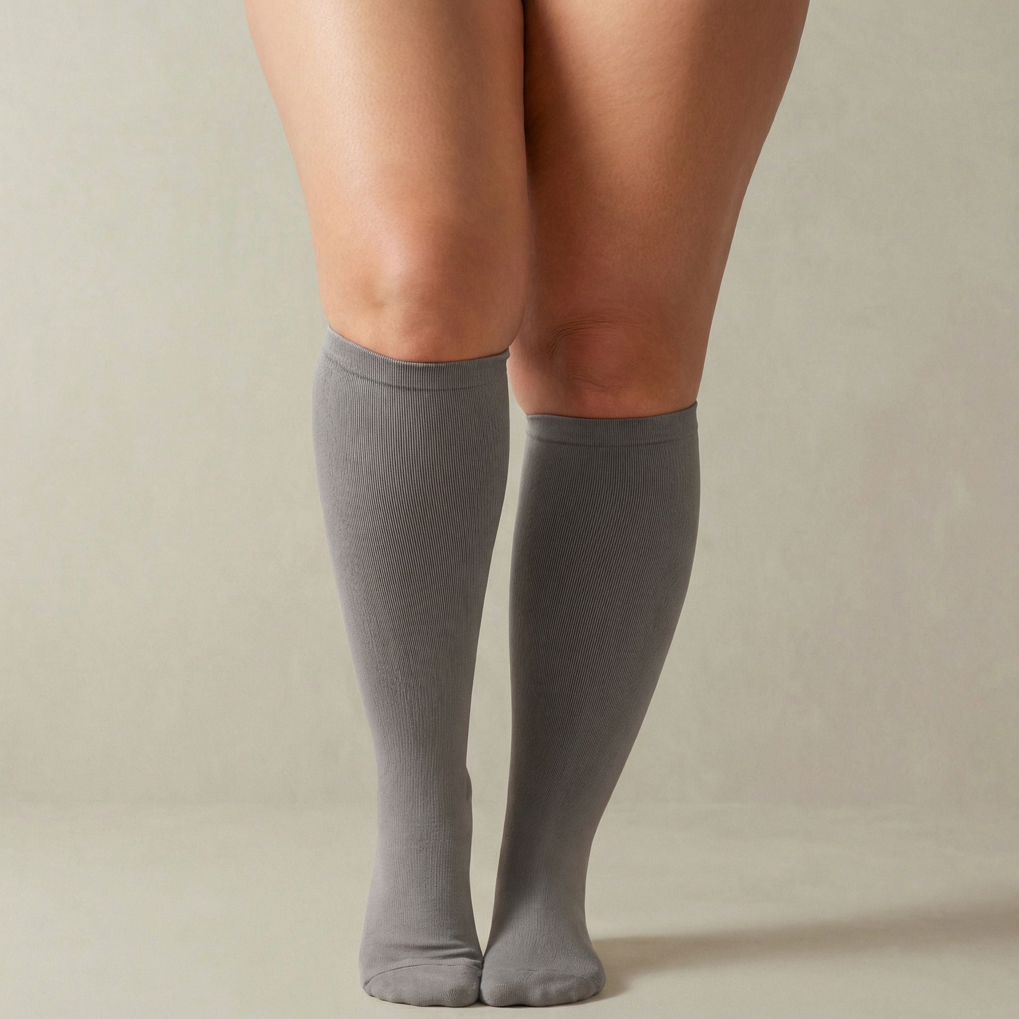 Gray knee-high compression socks worn by a person on a beige background