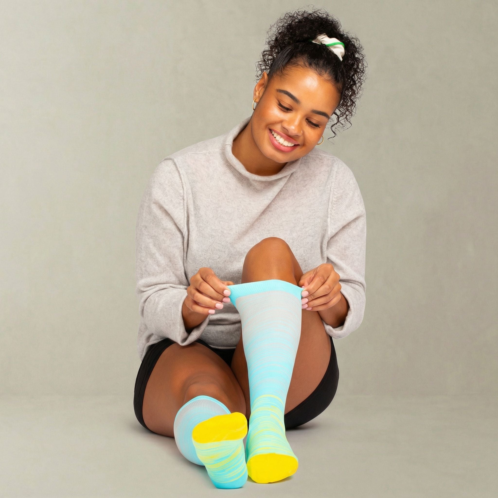 Woman sitting and holding a pair of colorful compression socks against a plain background