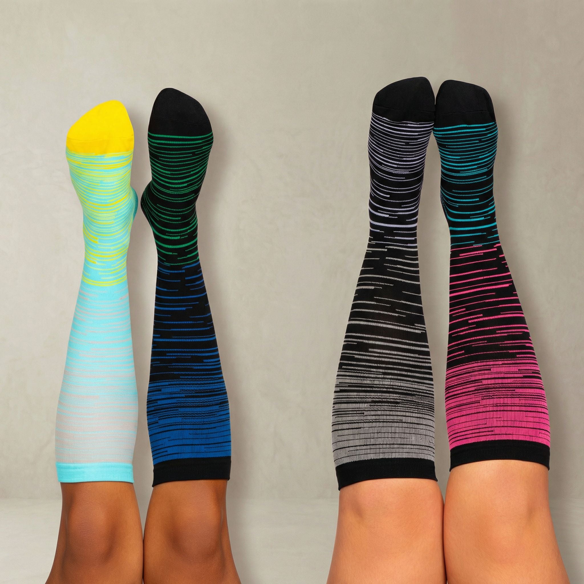 Two pairs of colorful knee-high compression socks on legs against a neutral background
