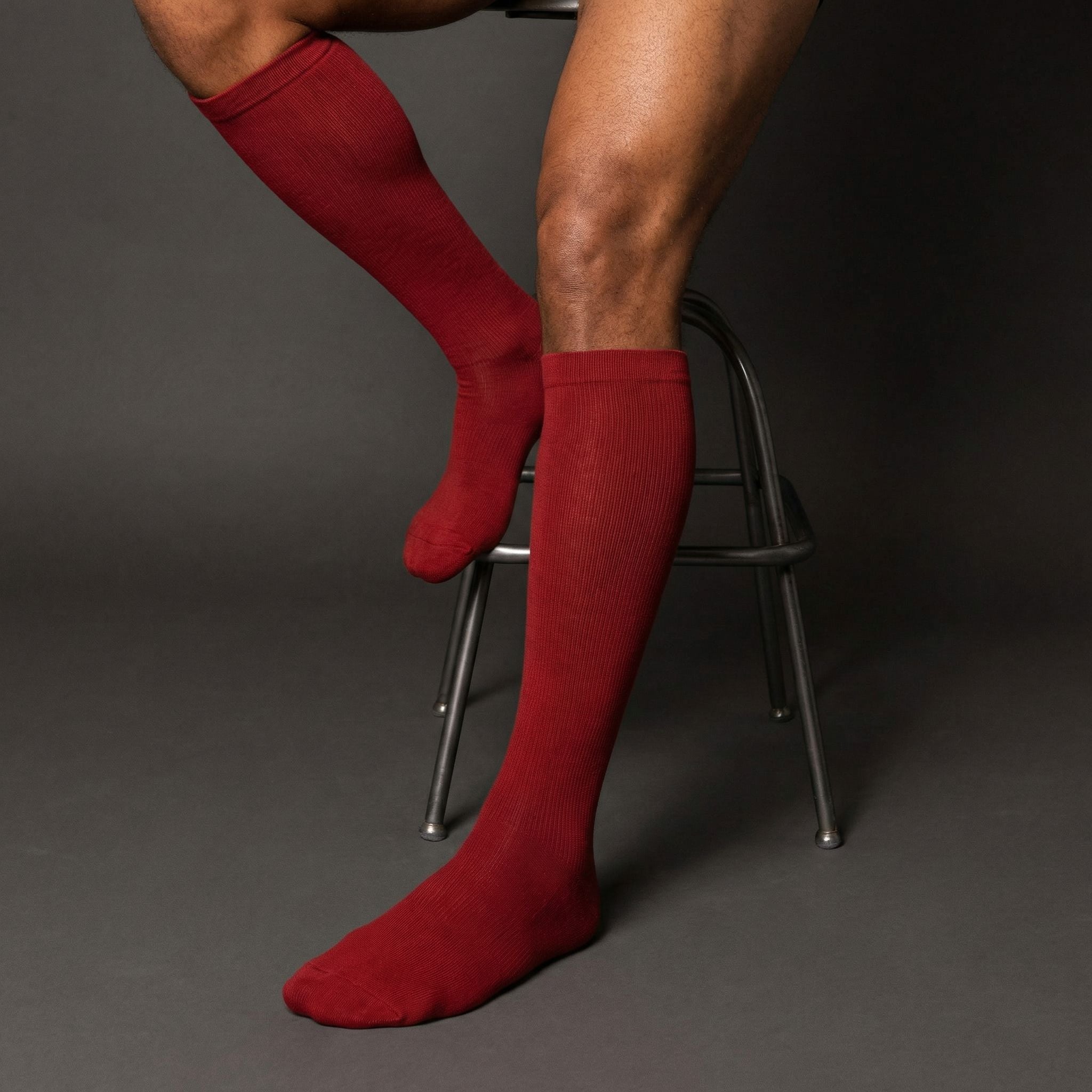 Burgundy compression knee-high socks worn by a person sitting on a chair against a gray background