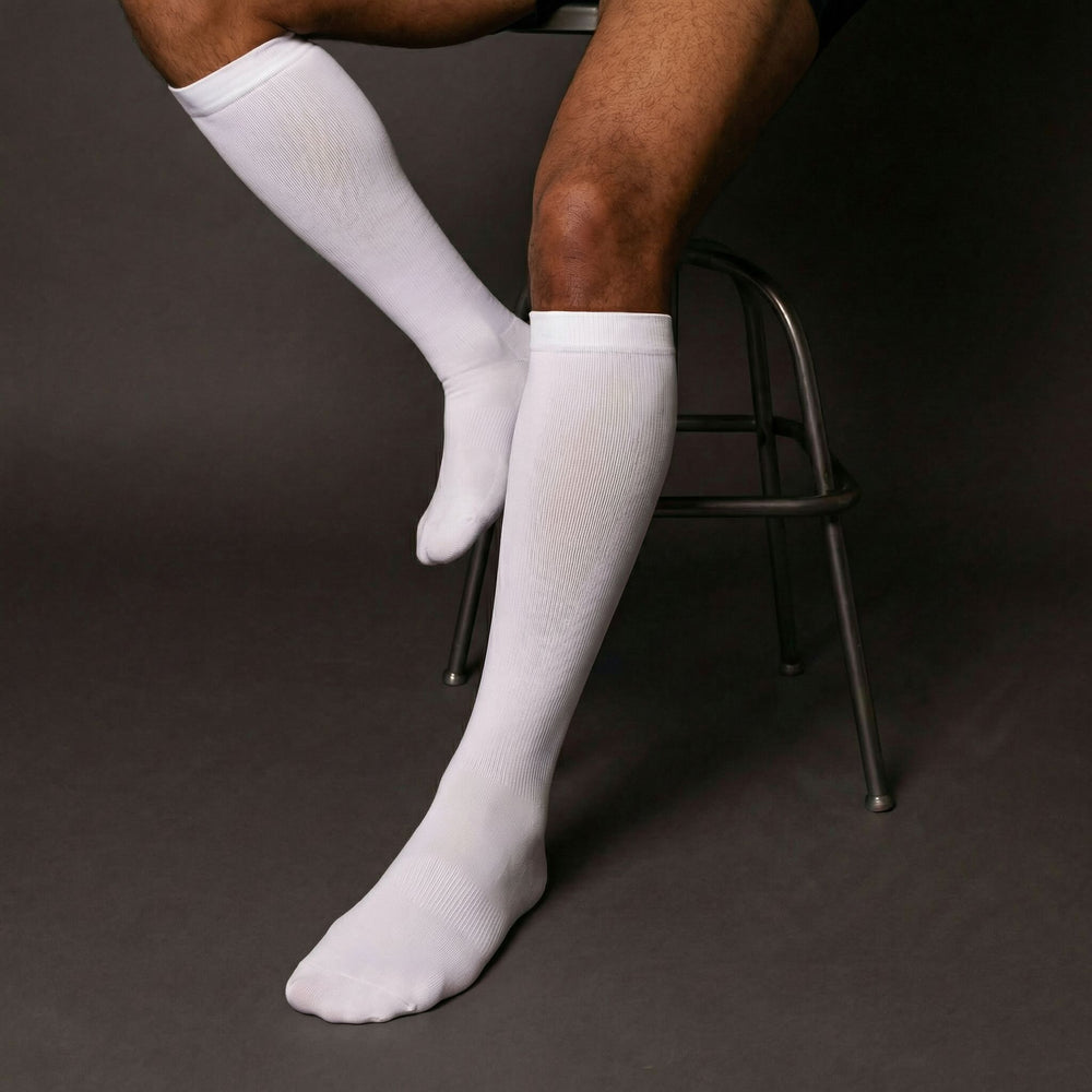 Person wearing white compression knee-high socks sitting on a chair against a dark background